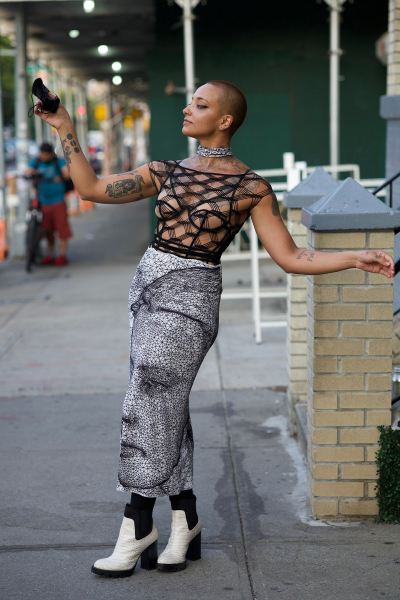 woman with short hair posing outside in mesh seethrough shirt and skirt with a face printed on it